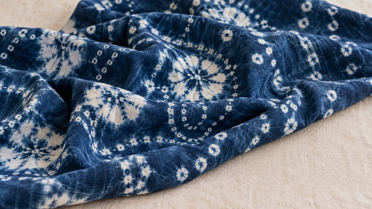 Blue-and-white tie-dyed cotton fabric with floral patterns draped in soft folds on an ivory surface.