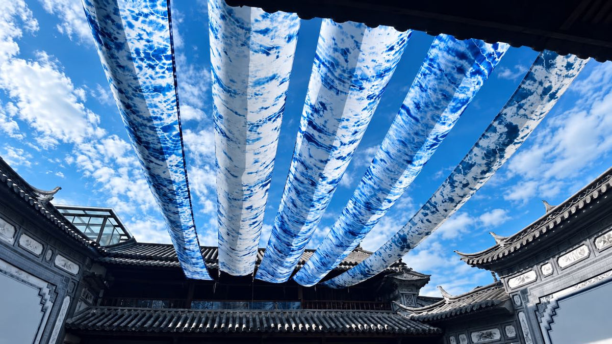 Blue-and-white dyed fabric hangs overhead in a traditional Chinese courtyard under a blue sky.